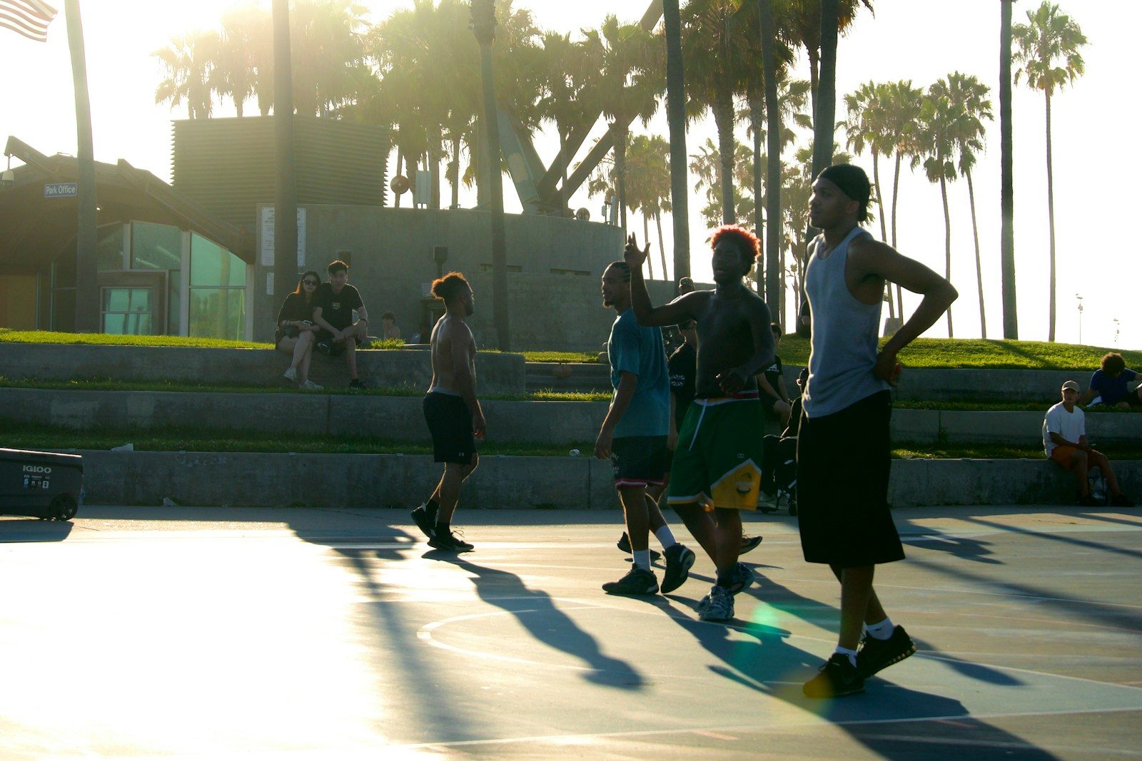 A group of people playing basketball on an outdoor court with palm trees